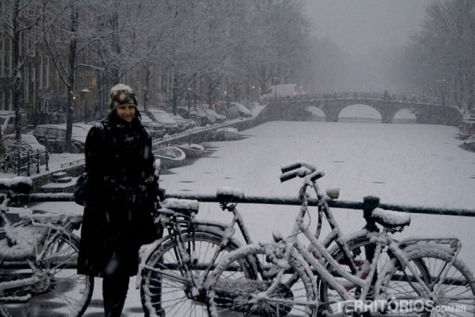 Mulher em frente ao canal coberto de gelo indica Amsterdam para viajar em dezembro