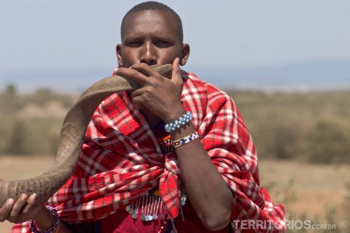 Masai tocando instrumento de chifre protegido com o shuka vermelho (tradicional cobertor)