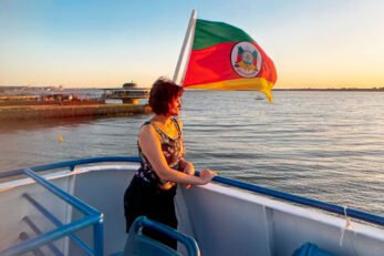 Mulher aprecia pôr do sol no Guaíba com bandeira do Rio Grande do Sul