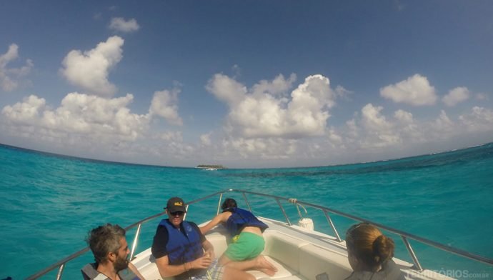 Pessoas em lancha para conhecer San Andrés, em direção à ilha. Céu azul com nuvens, mar com diferentes tons de verde.