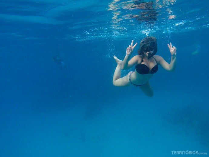 Mulher de biquíni mergulha no mar azul com snorkel e faz sinal de vitória com as mãos. Durante o passeio de lancha para conhecer San Andrés.
