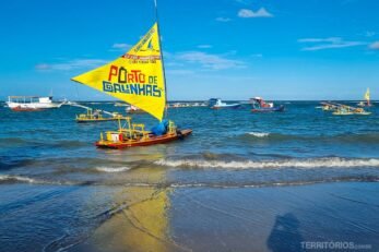 Jangada com vela amarela escrito Porto de Galinhas na beira da praia em um dia de céu azul