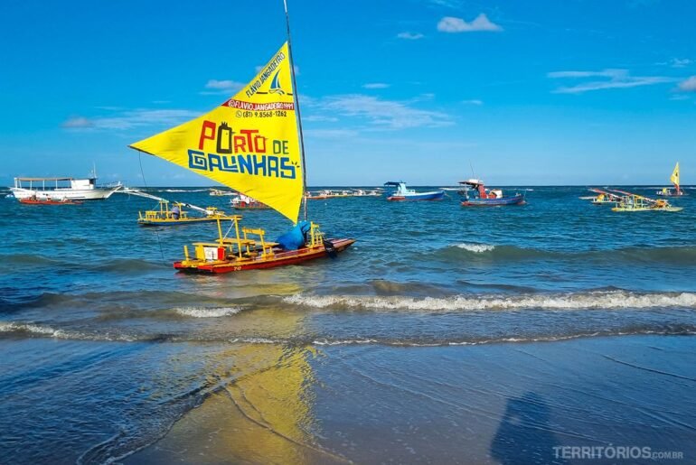 Jangada com vela amarela escrito Porto de Galinhas na beira da praia em um dia de céu azul