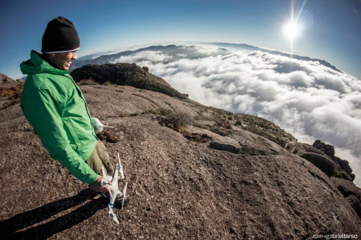 As montanhas mais altas do Brasil e Drone da Montanha – Entrevista com Samuel Oscar Homem com drone da mão sorri e observa a paisagem acima das nuvens do alto de uma montanha