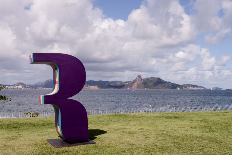 Como? Onde? Quando? Setembro em eventos Letra R estlizada em cor roxa em gramado em frente a cenário com água e montanha no mês de setembro