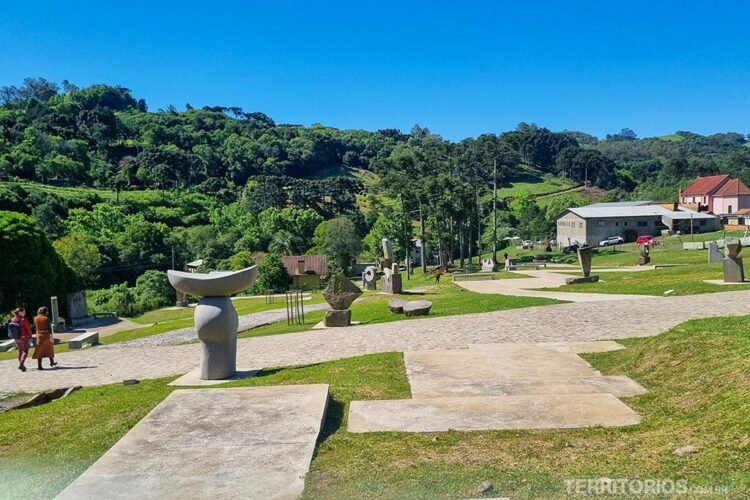 Parque com várias esculturas de basalto, caminhos pavimentados e vegetação abundante ao fundo