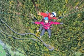 Homem e mulher voam de parapente sobre uma floresta, eles olham para cima felizes para a foto