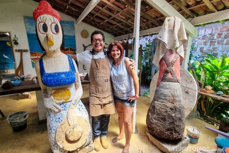 O artista Carcará abraça Roberta no seu ateliê onde produz as galinhas gigantes feitas do tronco do coqueiro