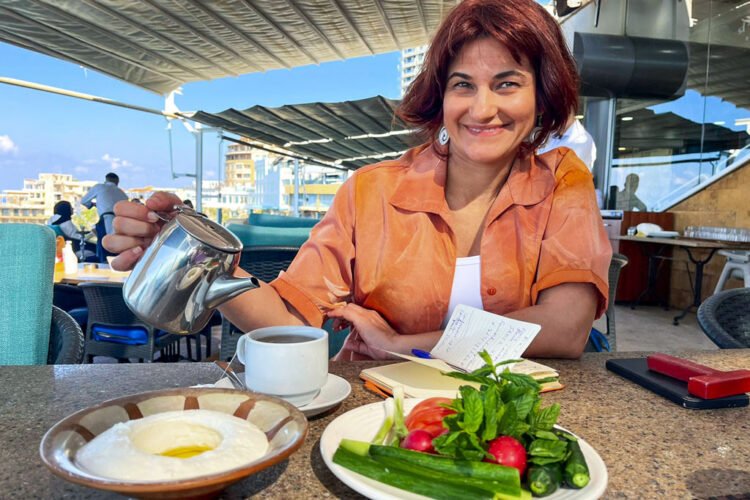 Mulher morena vestindo camisa laranja toma chá com iogurte e vegetais em cafeteria
