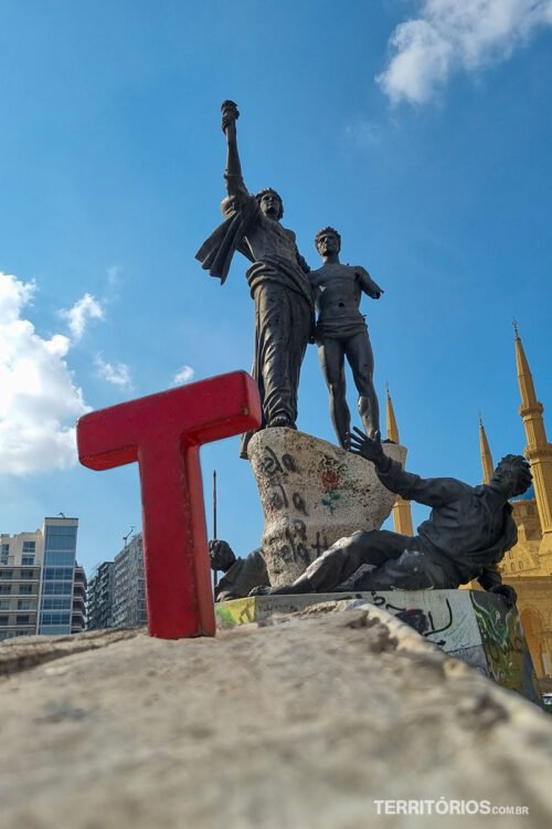 Letra T (Tesão) de madeira em frente a estatua