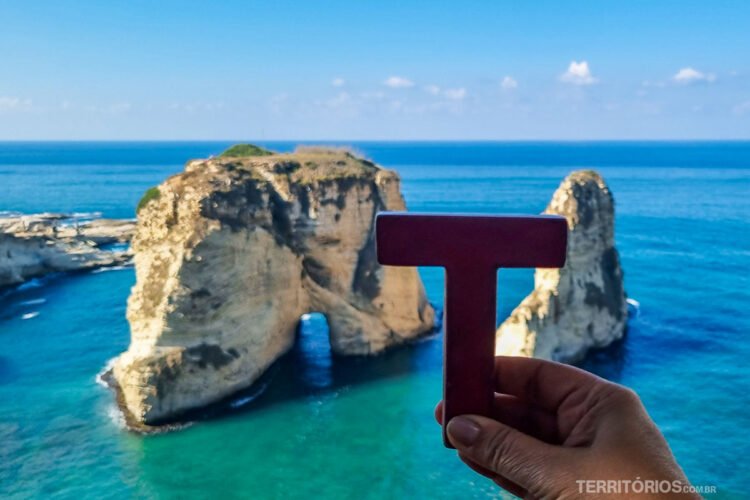 Letra T (Tesão) de madeira em frente as rochas do Mar Mediterrâneo azul com céu azul