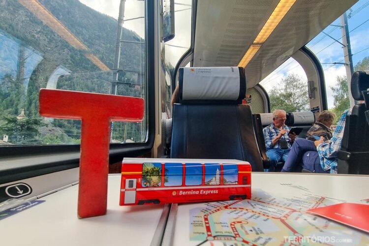 Letra T (Tesão) de madeira ao lado de embalagem de metal da Bernini Express no trem de mesmo nome