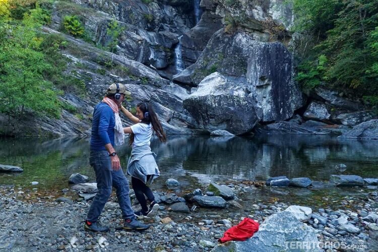 Homem e mulher dançam com fones de ouvido em frente a um lago e rochas. Experiência sensacional na Suíça