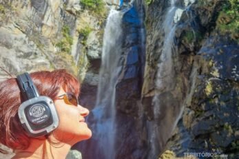 Mulher com fone de ouvido em frente a cachoeira e parede rochosa
