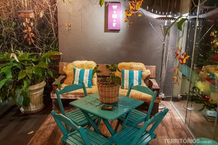 Ambiente com plantas, mesa azul, cadeiras com pelego e almofada. Opção de hospedagem no Vale Germânico