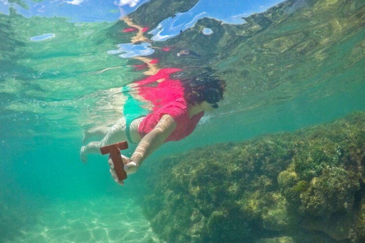 Mulher mergulha nos recifes e segura letra T vermelha