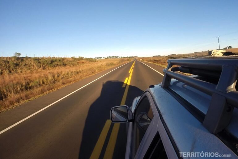 Carro em movimento na estrada plana. Céu azul no horizonte.