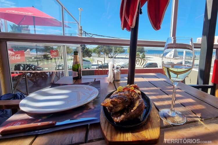 Mesa em terraço com prato de carne e taça de vinho. Restaurante em Puerto Madryn