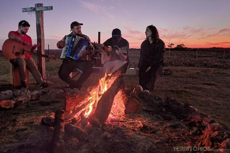 Pôr do sol com fogueira e músicos com instrumentos no norte do Uruguai