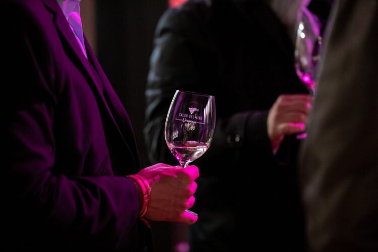 Homens seguram taças de vinho em ambiente escuro do salão do vinho em junho