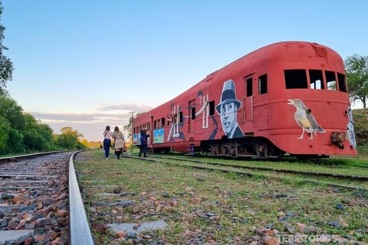 Carcaça de trem vermelho com grafites e linha férrea no norte do Uruguai