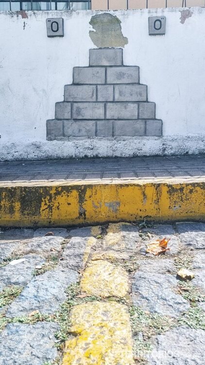 Linha do Equador representada com pintura amarela no paralelepípedo e tijolos na parede 