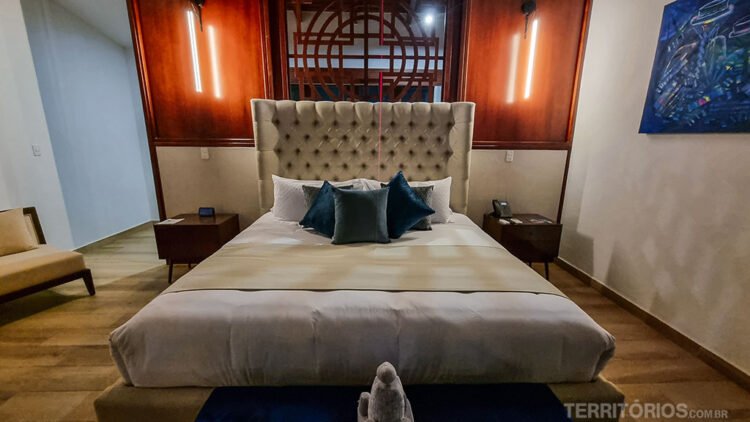 Quarto de hotel com destaque para a cama de casal no centro.