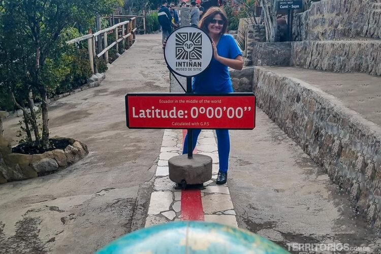 Mulher veste azul atrás de placa indicando Linha do Equador
