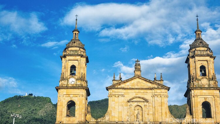Igreja antiga em pedra, ao fundo cerro, céu azul e nuvens. Destaque do turismo na Colômbia.