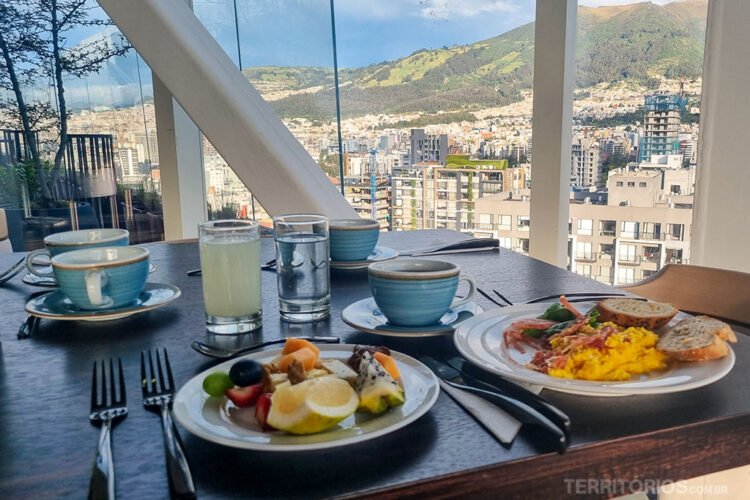Mesa servida com café da manhã do Go Quito Hotel próxima à janela com vista para cidade e montanha