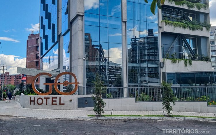 Fachada do Go Quito Hotel com letreiro e calçada. Céu azul com nuvens.