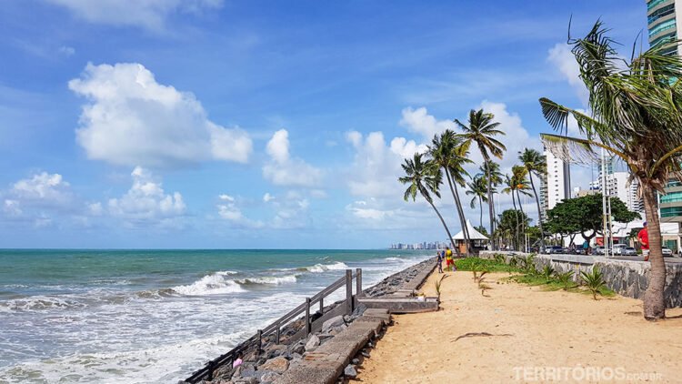 Praia de Boa Viagem, no Recife, com coqueiros, areia, maré alta e céu azul com nuvens
