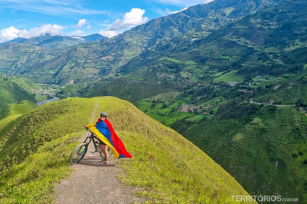 Mulher em bicicleta envolta em bandeira em cenário verde de montanhas para promover o turismo na Colômbia