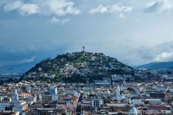 Indice Equador, centro de Quito com colina no meio. Céu azul com nuvens.