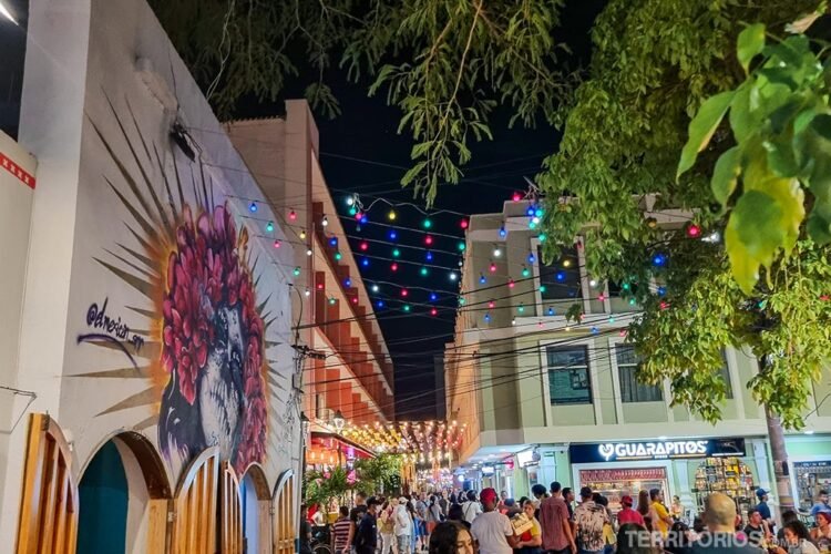 Rua movimentada e iluminada no centro de Santa Marta. Luzes coloridas e grafites