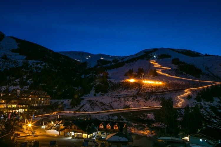 Foto noturna com luzes amarelas iluminando caminhos na montanha de neve para evento em agosto