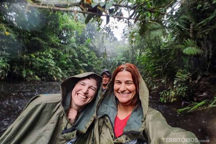 Duas mulheres sorridentes vestem ponchos verdes enquanto navegam na selva com chuva