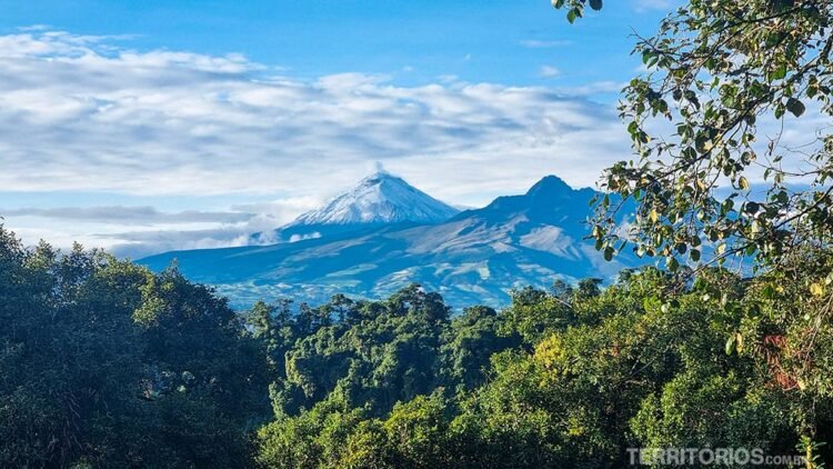 Vulcão Cotopaxi, montanhas e árvores. Céu azul entre nuvens.