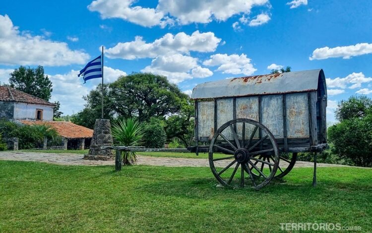 Carroça antiga no gramado verde ao lado da bandeira em clima no Uruguai