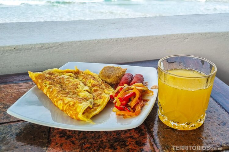 Omelete com salsicha e molho de pimentão e cebola servido em prato branco ao lado do copo de suco de laranja