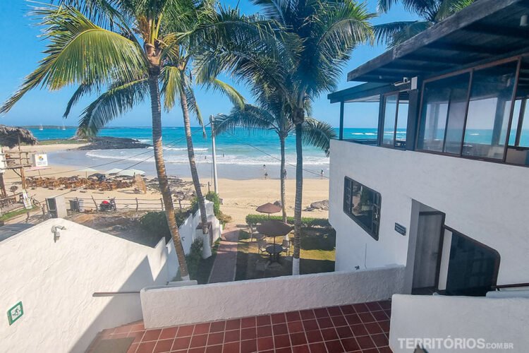 Vista de uma sacada branca de hotel em Isabela para a praia com coqueiros, jardim e mar azul cintilante.