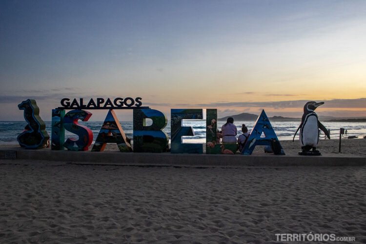 Letreiro na praia escrito Galapagos Isabela com mapa da ilha de uma lado e escultura de pinguim do outro