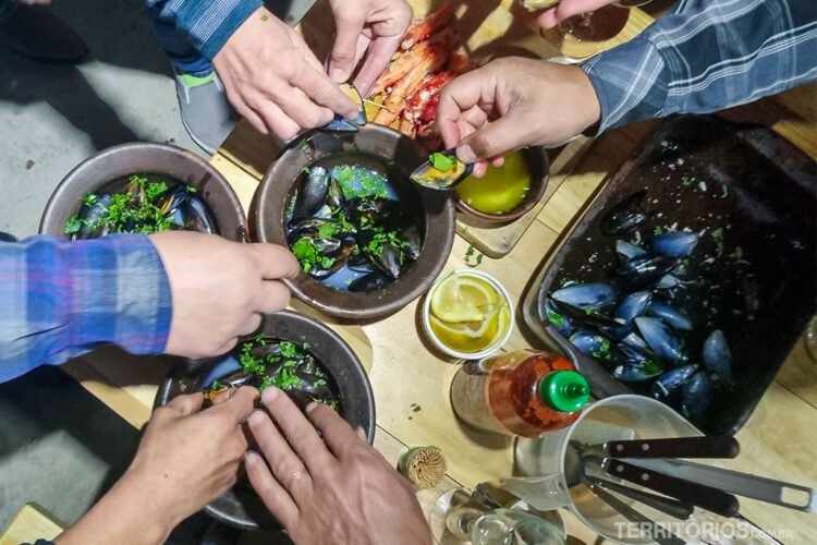 Várias mãos pegam comida em pratos com frutos do mar frescos de Puerto Natales em uma mesa de madeira.