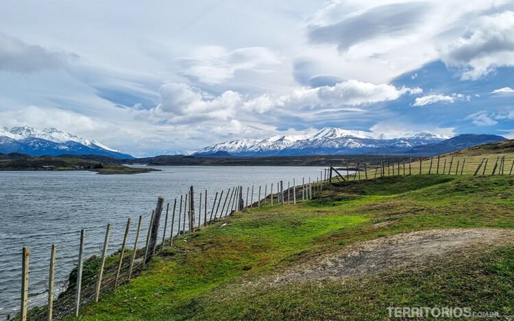 Campo verde cercado por cerca de madeira e arame para o mar rodeado por montanhas nevadas ao redor de Puerto Natales