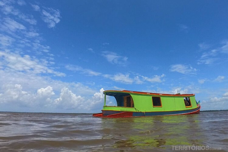 Barco colorido navega pelo rio Amazonas com céu azul e poucas nuvens