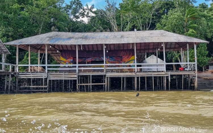 Casa palafita com paredes pintadas com grafite sobre o rio. Atrás vegetação densa e céu azul na Ilha do Combú