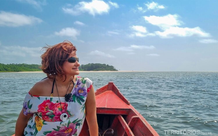 Mulher morena de óculos escuros e blusa florida observa a paisagem de um barco navegando em rio na Ilha do Marajó