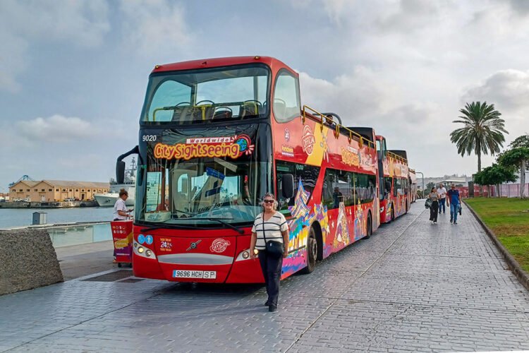 Mulher faz pose em frente a ônibus de turismo vermelho em dia nublado