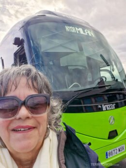 Mulher de cabelo branco e curto usa óculos escuro em frente ao ônibus verde da FlixBus