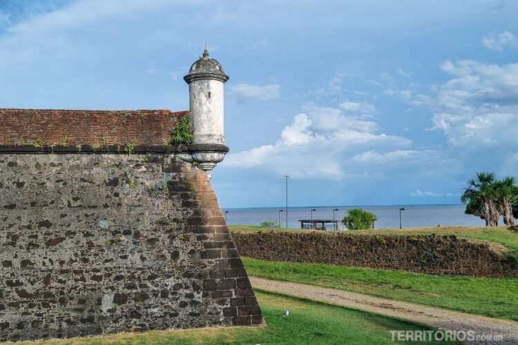 Muralha de pedra da Fortaleza de São José de Macapá e vista para o rio Amazonas. Céu azul com nuvens.